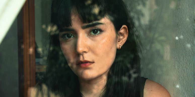 A woman looking thoughtful through a window, reflecting emotional distance and inner conflict in a relationship