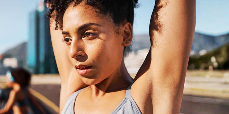 A woman stretching her arms overhead outdoors in an urban setting.