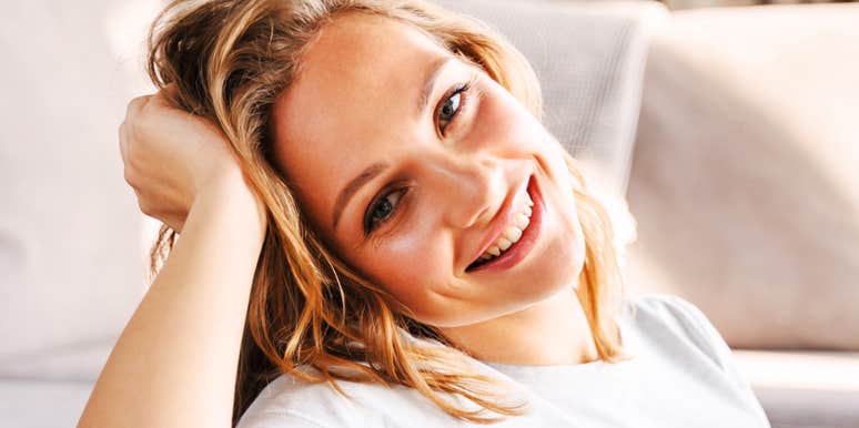 A woman smiling while resting her head on her hand indoors.