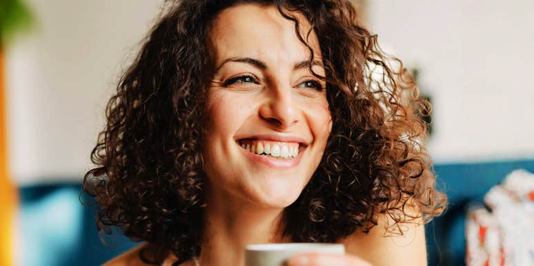 Smiling woman with curly hair holding a coffee cup in soft natural light