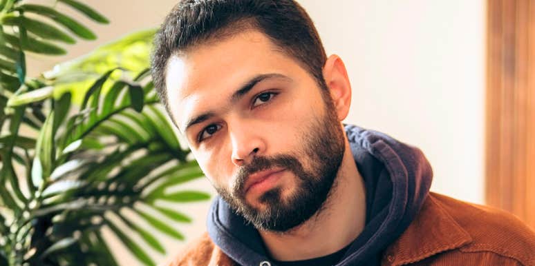 A thoughtful man looking at his phone indoors, appearing uncertain, reflecting modern texting habits that can unintentionally stall conversations.