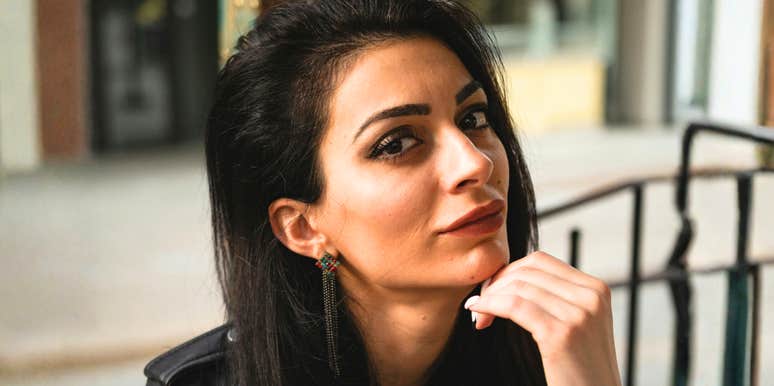 A woman with dark hair resting her chin on her hand outdoors.