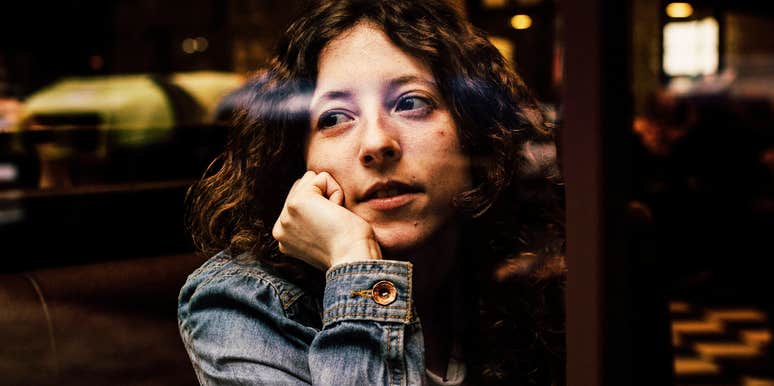 person sitting alone at a café, resting their chin on their hand and gazing out the window thoughtfully