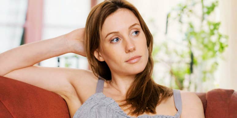 thoughtful woman sitting alone on a couch with distant gaze, soft natural light highlighting quiet strength and resilience during life transition after divorce