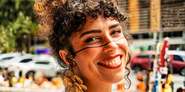 Confident woman smiling warmly outdoors in natural light, casual candid portrait capturing authentic self-assurance and quiet strength that earns genuine respect