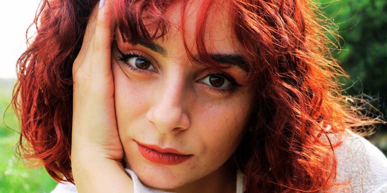 close-up of thoughtful red-haired woman resting her face in her hand outdoors