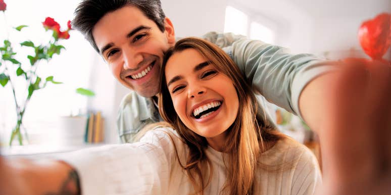 smiling couple taking a joyful selfie at home, laughing together in warm natural light