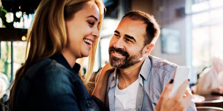 Man smiling at a woman as they look at a phone together indoors.