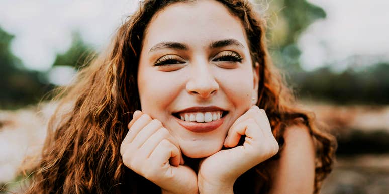 Smiling woman resting her chin on her hands, looking content and relaxed.
