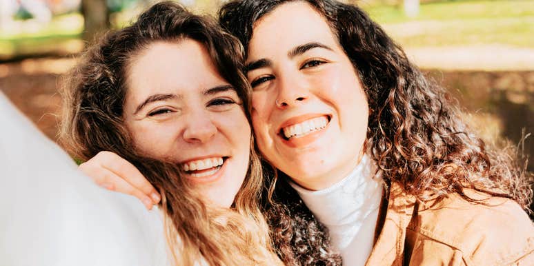 Two women smiling together outdoors, posing closely for a photo.