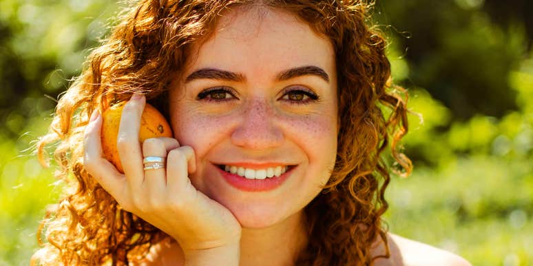 close-up of radiant young woman with curly red hair smiling in golden sunlight