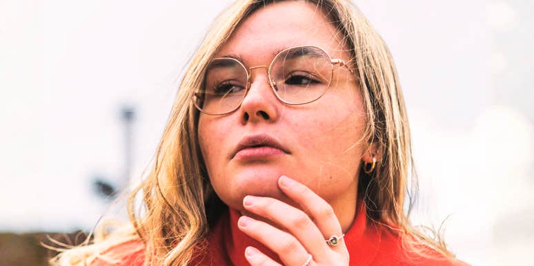 A person wearing glasses with their hand near their face outdoors