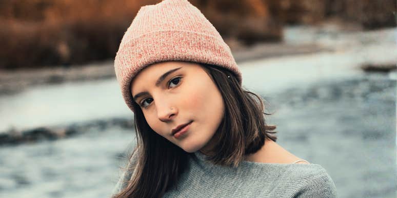 Woman outdoors wearing a grey sweater and pink beanie, head tilted, illustrating how communication style can influence attraction