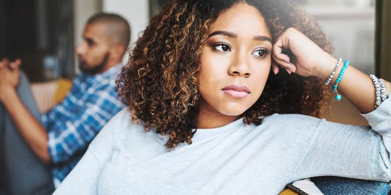 thoughtful woman sitting on a couch with distant partner blurred in the background