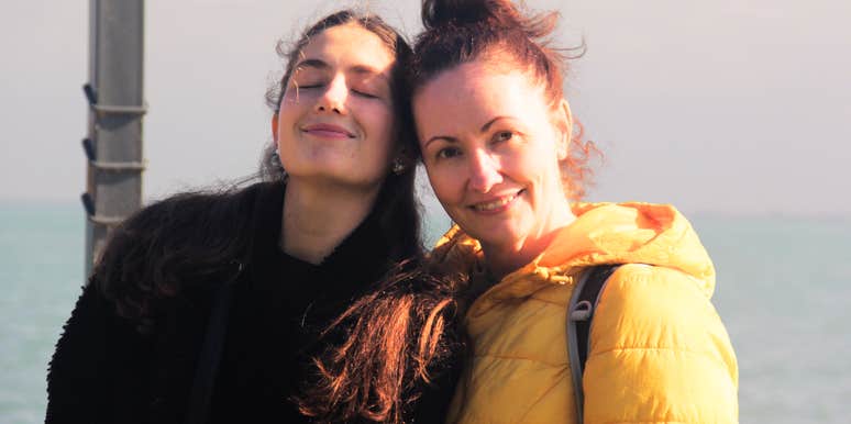 Mother looking at the camera while her daughter smiles with closed eyes, reflecting lessons in self-respect and confidence