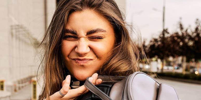 A woman smiling while holding a backpack outdoors.