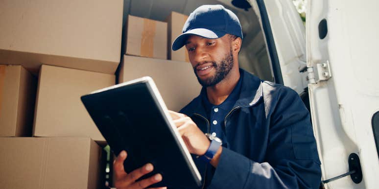 delivery courier using tablet standing in back of van with boxes