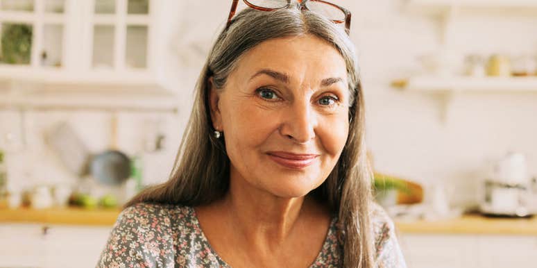 A pretty grey-haired woman in a flowered dress smiling radiantly in her kitchen, embodying the sense of freedom and clarity that comes when trivial worries stop mattering in your sixties.