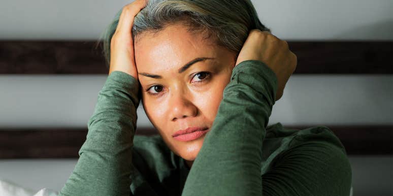 A mature woman looking thoughtful and vulnerable in a bedroom setting, illustrating the quiet struggle with negative self-talk and the 'small changes' experts recommend for mental wellness.