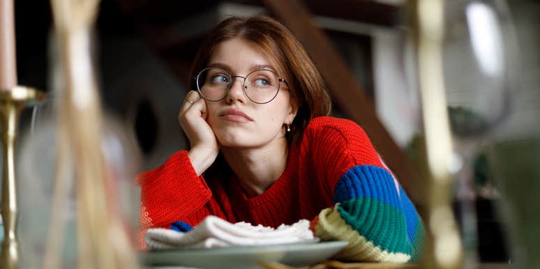 bored young woman sitting at desk with hand on cheek