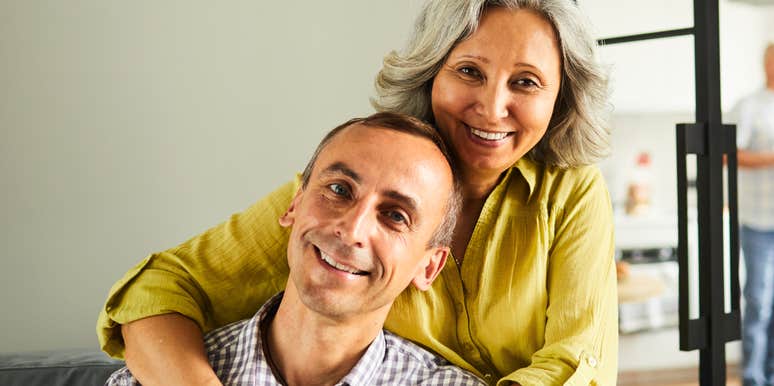 A portrait of a vibrant man and woman in their sixties sharing a moment of physical closeness, representing the 'secure attachment' and mutual support found in enduring partnerships.