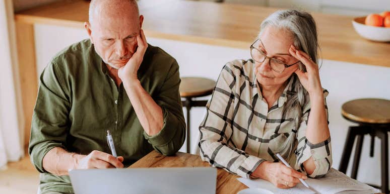 A couple in their sixties looking focused and concerned while budgeting at home, illustrating the 'financial vigilance' required to manage stress in later life.