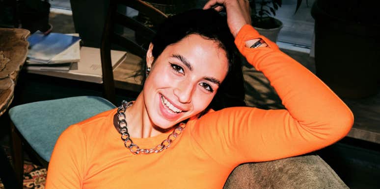 smiling woman in bright orange sweater leaning back thoughtfully, relaxed confident expression
