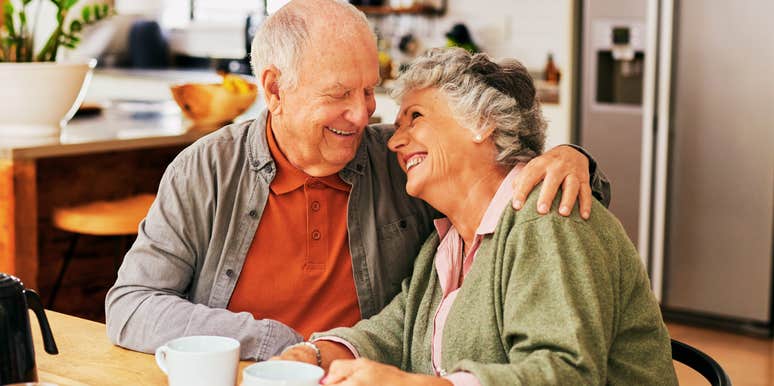 A happy senior couple sharing a tender embrace and laughing over coffee, illustrating the deep affinity and personal transformation that comes from decades of a successful marriage.