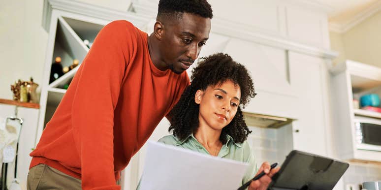 A multiracial couple sitting together at home using a tablet for online banking, illustrating the 'collaborative mindset' and mental shifts used to manage financial anxiety.
