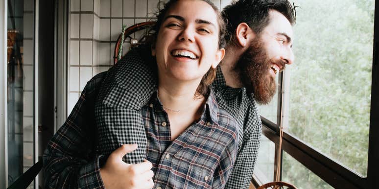 Playful couple laughing as a man hugs a woman from behind, illustrating how someone others doubt could still become your happiest relationship