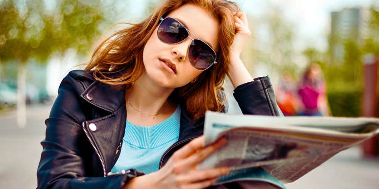 Adult child of divorce wears glasses and looks serious on a park bench with a paper