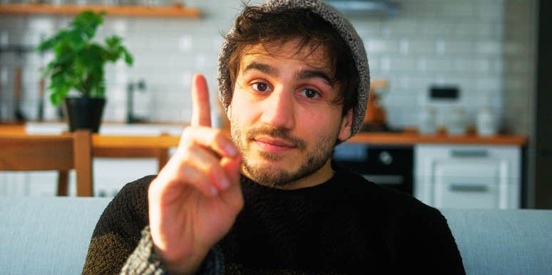 A young man with a beanie on a sofa, captured mid-sentence as he interrupts a conversation, illustrating the common communication mistake men make without realizing it.