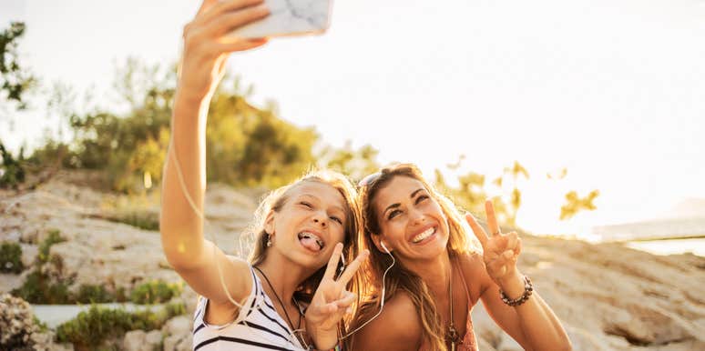 A happy teenage girl and her mother take a sunset selfie on a beach, representing the fleeting moments of connection amidst the hidden challenges of raising teens.