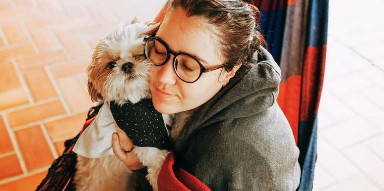 A stylish woman relaxing on a hammock with her dog in a warm, domestic embrace; illustrating the deep emotional attachment and 'baby-like' care that modern pet owners provide to their companions. 