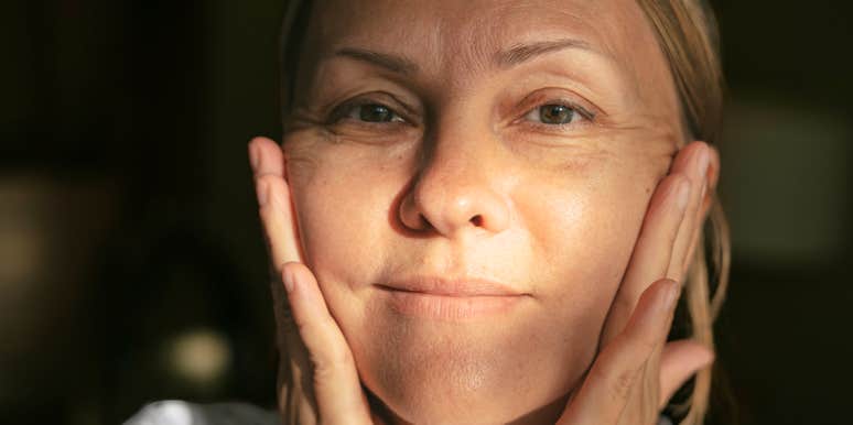 A portrait of a middle-aged woman touching her face with a thoughtful expression.