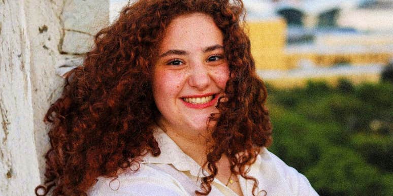 A portrait of a woman with vibrant curly red hair smiling genuinely; illustrating the approachable and compassionate nature of individuals who practice habits of kindness in challenging situations.