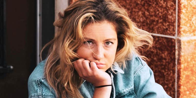 A portrait of a tired woman with wind-blown hair resting her chin on her hand; a visual representation of the subtle signs of long-term stress that many women brush off as ordinary.