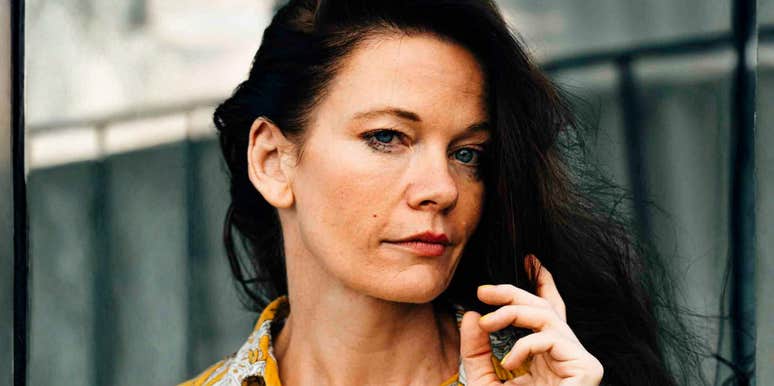A portrait of an elegant woman in her fifties wearing a vibrant yellow shirt.