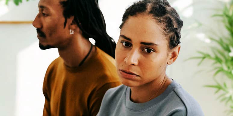 An unhappy couple sits side-by-side on a bed, physically close but emotionally distant, illustrating the "alone together" signs common in struggling relationships.
