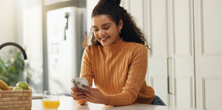 smiling woman texting on smartphone in kitchen