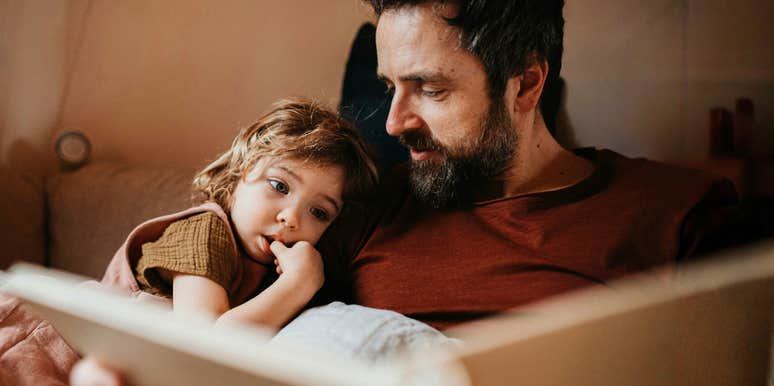 A father reading to his daughter, illustrating the 'joint attention' and emotional signaling that builds empathy in early childhood.