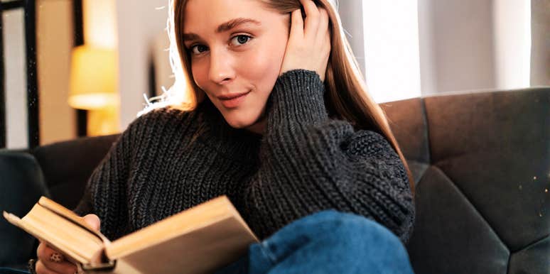 An expressive young woman holding a book and looking into the camera, representing the deep empathy and rare personality traits of readers who bond with fictional characters.