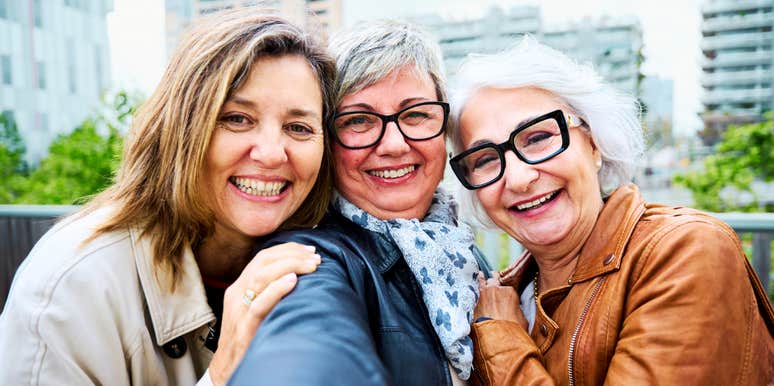 Three joyful mature women over fifty taking a city selfie, illustrating the profound life improvement and happiness that comes from lifelong female friendships.