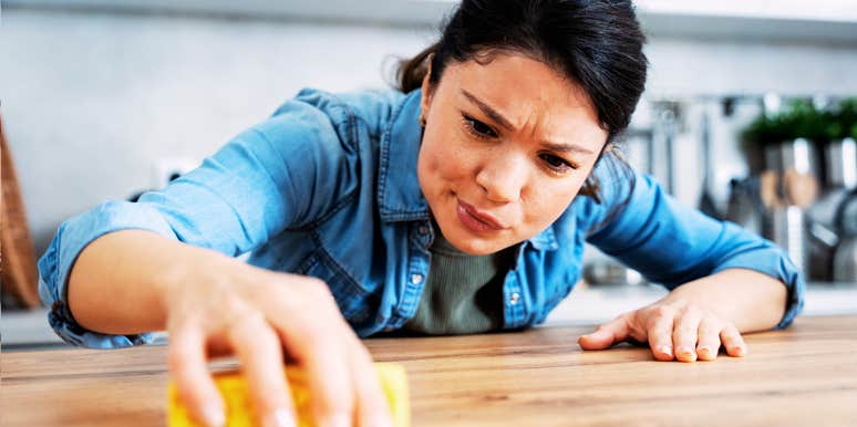 A young woman obsessively cleaning a kitchen surface with a sponge; a visual representation of how meticulous home maintenance acts as a subconscious coping mechanism for stress.
