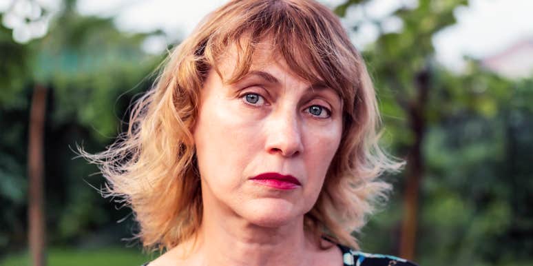 A somber middle-aged woman with blonde hair looking pensive; illustrating the "unseen" parts of getting divorced in your 50s, from social changes to the dismantling of a long-term family unit.