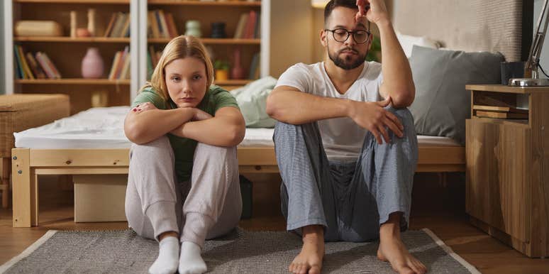upset couple sitting next to bed on floor