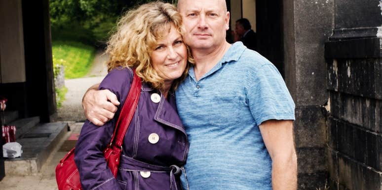 A happy woman in her fifties standing with her husband, reflecting the freedom of letting go of body insecurities and celebrating the 'softness' that comes with age.
