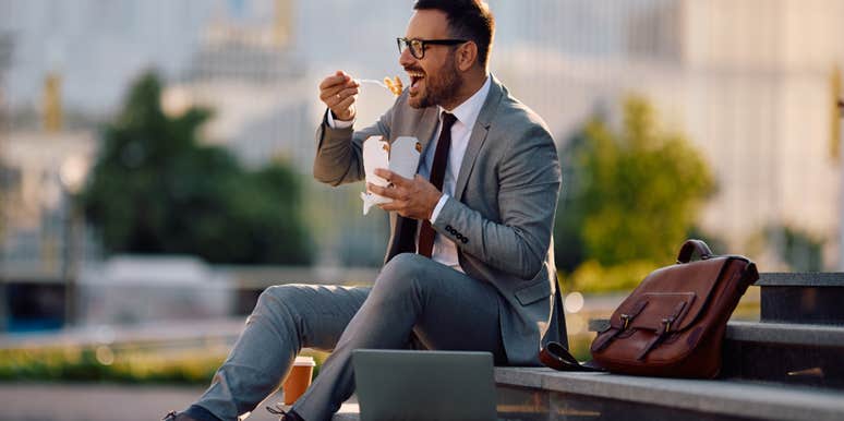 businessman eating takeout with chopsticks on steps outside