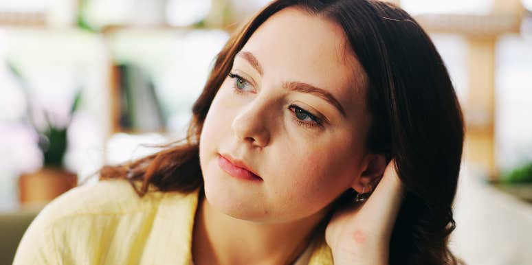 A pensive woman reflecting on her sofa in a living room; illustrating the long-term psychological effects and personality traits formed when a child grows up without experiencing parental remorse.