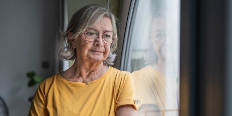 elderly woman standing next to window